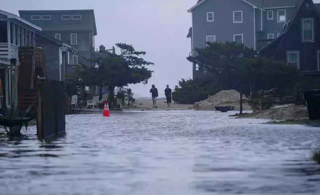 People look out at a flooded road in the midst of a storm, Sunday, Oct. 12, 2025, in Buxton, N.C. (AP Photo/Allison Joyce)