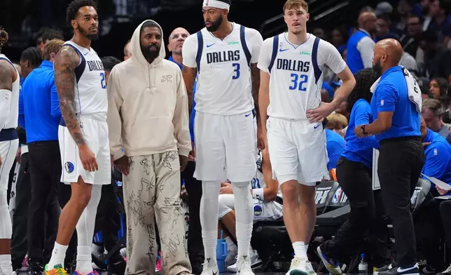 Dallas Mavericks teammates Cooper Flagg (32), Anthony Davis (3), Kyrie Irving, second from left, and P.J. Washington (25) look on from the bench area during a timeout in the second half of an NBA basketball game against the San Antonio Spurs in Dallas, Wednesday, Oct. 22, 2025. (AP Photo/LM Otero)