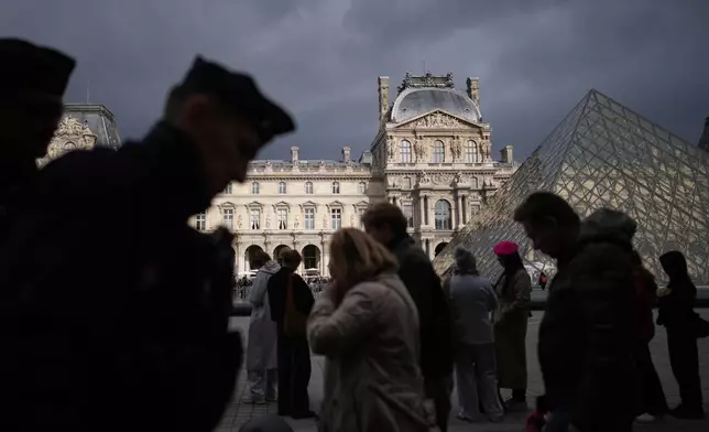 Police officers, left, patrol as people queue to enter Le Louvre museum Monday, Oct. 27, 2025 in Paris. (AP Photo/Christophe Ena)