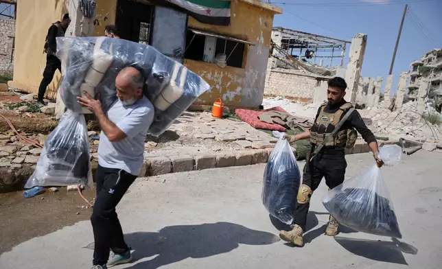 A Syrian government soldier assists a man carrying his belongings as residents leave the Sheikh Maqsoud and Achrafieh neighborhoods of Aleppo, Syria, Tuesday, Oct. 7, 2025, following overnight clashes between Syrian government troops and the Kurdish-led Syrian Democratic Forces. (AP Photo/Omar Albam)