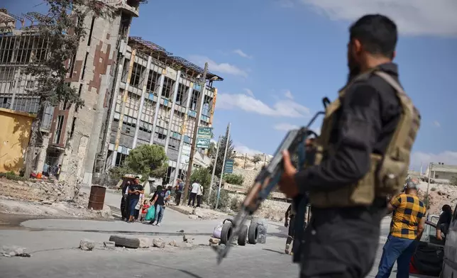 Syrian security forces stand guard as residents leave the Sheikh Maqsoud and Achrafieh neighborhoods of Aleppo, Syria, Tuesday, Oct. 7, 2025, following overnight clashes between Syrian government troops and the Kurdish-led Syrian Democratic Forces. (AP Photo/Omar Albam)