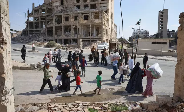 Residents walk past a security forces checkpoint as they leave the Sheikh Maqsoud and Achrafieh neighborhoods of Aleppo, Syria, Tuesday, Oct. 7, 2025, following overnight clashes between Syrian government troops and the Kurdish-led Syrian Democratic Forces. (AP Photo/Omar Albam)