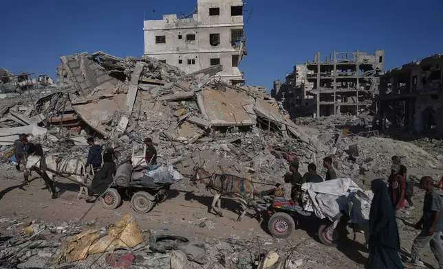 Displaced Palestinians ride donkey carts loaded with belongings past destroyed buildings in Gaza City, Saturday, Oct. 11, 2025, after Israel and Hamas agreed to a pause in their war and the release of the remaining hostages. (AP Photo/Abdel Kareem Hana)