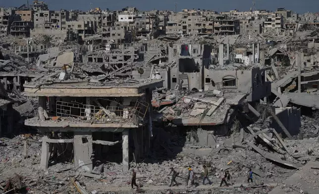 Displaced Palestinians walk through an area surrounded by destroyed buildings in Khan Younis, in the southern Gaza Strip, Saturday, Oct. 11, 2025, after Israel and Hamas agreed to a pause in their war and the release of the remaining hostages. (AP Photo/Jehad Alshrafi)