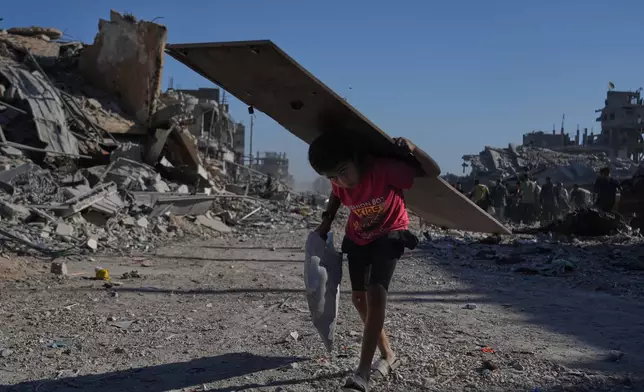 A displaced Palestinian boy carries a wooden board as he walks along the heavily damaged Al-Jalaa Street in Gaza City, Saturday, Oct. 11, 2025, after Israel and Hamas agreed to pause their war and release the remaining hostages. (AP Photo/Abdel Kareem Hana)