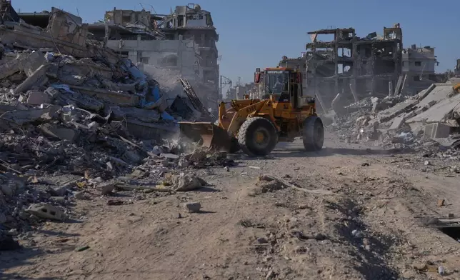 A Palestinian operates a mechanical shovel to clear a road surrounded by destroyed buildings in Khan Younis, in the southern Gaza Strip, Saturday, Oct. 11, 2025, after Israel and Hamas agreed to a pause in their war and the release of the remaining hostages. (AP Photo/Jehad Alshrafi)