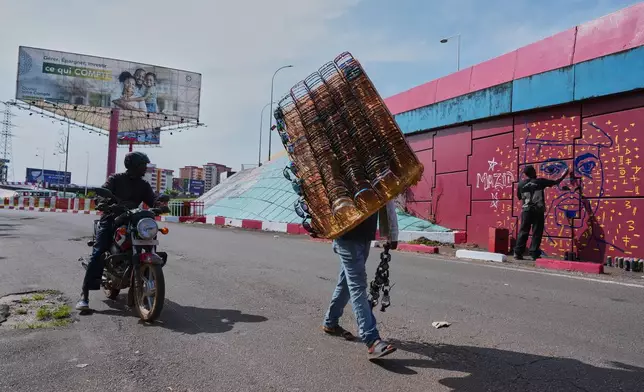 Passersby look on as graffiti artist Omar Diaw works on a mural depicting Guinea's President Mamadi Doumbouya on a street wall in Conakry, Guinea, Saturday, Sept. 20, 2025. (AP Photo/Misper Apawu)