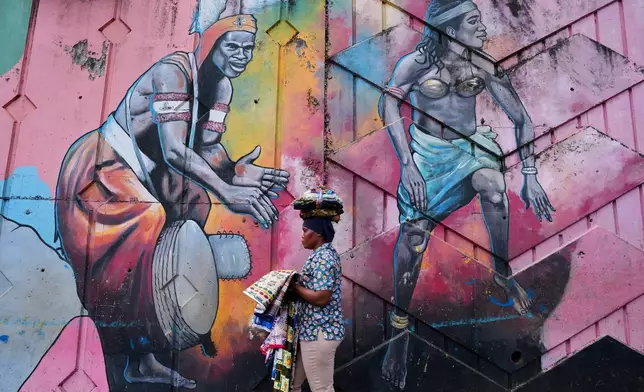 A street vendor walks past a mural depicting traditional dancers on a street wall in Conakry, Guinea, Saturday, Sept. 20, 2025. (AP Photo/Misper Apawu)