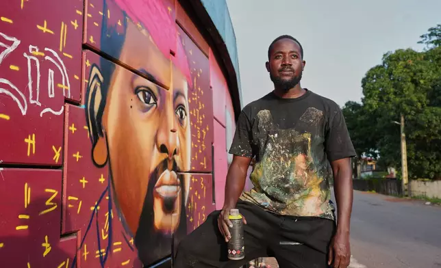 Graffiti artist Omar Diaw poses beside his mural depicting Guinea's President Mamadi Doumbouya on a street wall in Conakry, Guinea, Saturday, Sep. 20, 2025. (AP Photo/Misper Apawu)
