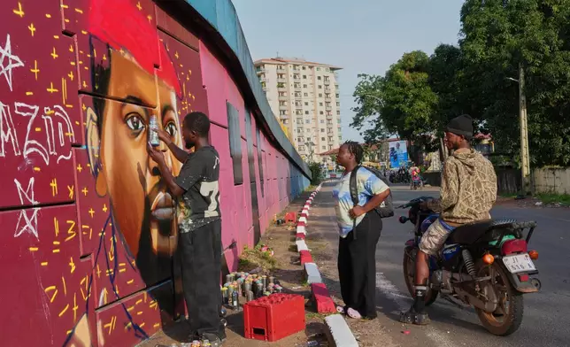Graffiti artist Omar Diaw paints a mural of Guinea's President Mamadi Doumbouya as people stop to look in Conakry, Guinea, Saturday, Sep. 20, 2025. (AP Photo/Misper Apawu)