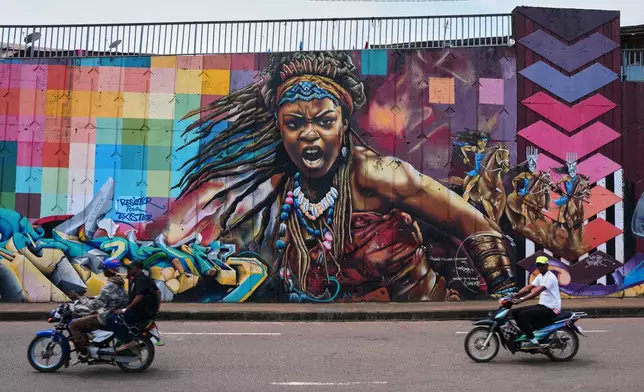 Motorcyclists ride past a mural depicting a powerful woman on a street wall in Conakry, Guinea, Sunday, Oct. 19, 2025. (AP Photo/Misper Apawu)