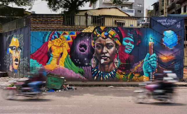 Motorcyclists ride past a mural painted by Graffiti artist Omar Diaw in Conakry, Guinea, Saturday, Sep. 20, 2025. (AP Photo/Misper Apawu)