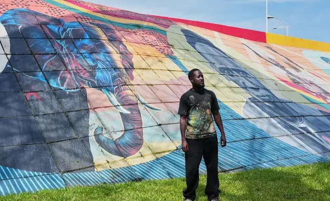 Graffiti artist Omar Diaw stands In front of one of his murals in Conakry, Guinea, Saturday, Sep. 20, 2025. (AP Photo/Misper Apawu)