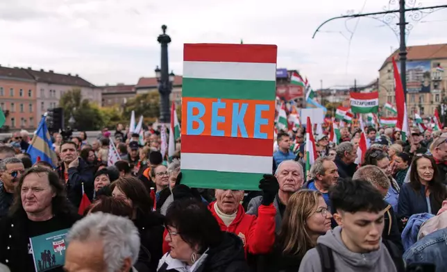 A pro-government demonstrator holds a sign reading "Peace" in Hungarian during celebrations marking the 69th anniversary of the outbreak of Hungary's 1956 revolution against communist rule and the Soviet Union, in Budapest, Hungary, Thursday, Oct. 23, 2025. (AP Photo/Rudolf Karancsi)