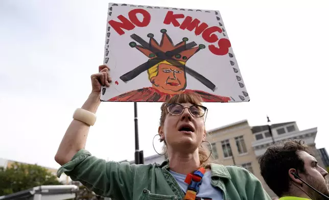 A demonstrator carries a sign as they rally at the 14th and U street corridor before marching to the national Mall during a No Kings protest in Washington, Saturday, Oct. 18, 2025. (AP Photo/Jose Luis Magana)