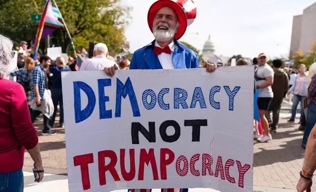 A demonstrtor carries a sign saying "DEMocracy not TRUMPocracy" on Pennsylvania Avenue during a No Kings protest in Washington, Saturday, Oct. 18, 2025. (AP Photo/Jose Luis Magana)