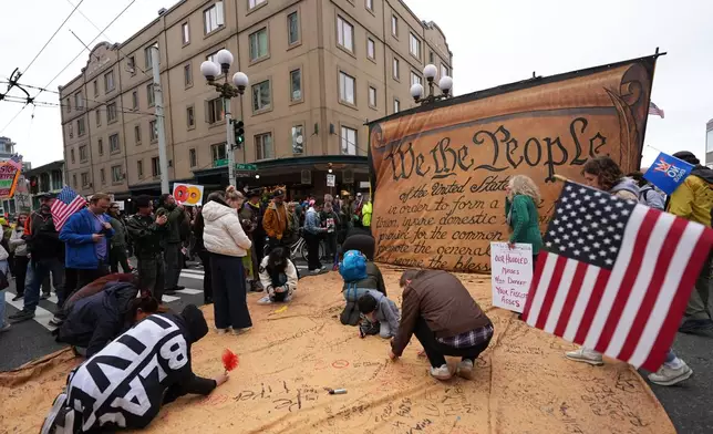 People are signing a giant Constitution as they take part in a "No Kings" protest Saturday, Oct. 18, 2025, in Seattle. (AP Photo/Lindsey Wasson)
