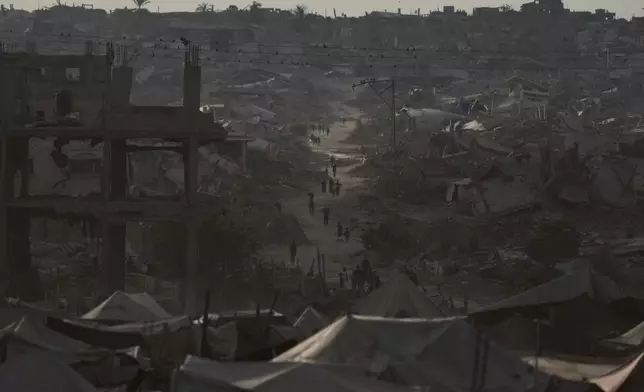 Displaced Palestinians walk trough destroyed homes and buildings in Khan Younis, Gaza Strip, Saturday, Oct. 18, 2025. (AP Photo/Jehad Alshrafi)