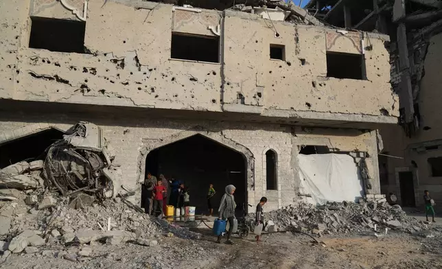 Displaced Palestinians collect water from a destroyed building in Khan Younis, Gaza Strip, Saturday, Oct. 18, 2025. (AP Photo/Jehad Alshrafi)