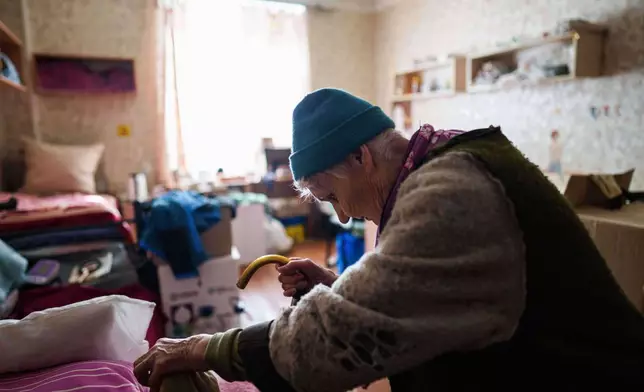 An elderly woman uses a cane to walk to her bed at a hostel for displaced people in Dnipro, Ukraine, Wednesday, Oct. 8, 2025. (AP Photo/Evgeniy Maloletka)