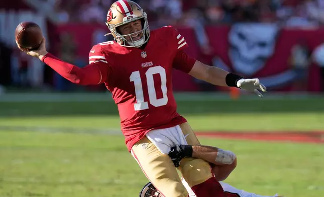San Francisco 49ers quarterback Mac Jones (10) passes the ball over Tampa Bay Buccaneers linebacker Anthony Nelson, bottom, during the first half of an NFL football game in Tampa, Fla., Sunday, Oct. 12, 2025. (AP Photo/Chris O'Meara)