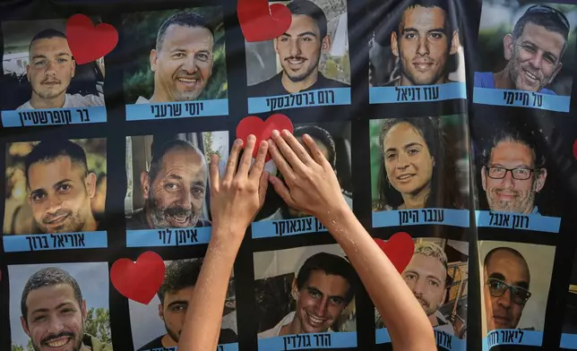 A person pastes a heart-shaped sticker on a banner with pictures of Israeli hostages during a a gathering at a plaza known as hostages square in Tel Aviv, Israel, Monday, Oct. 13, 2025. (AP Photo/Oded Balilty)