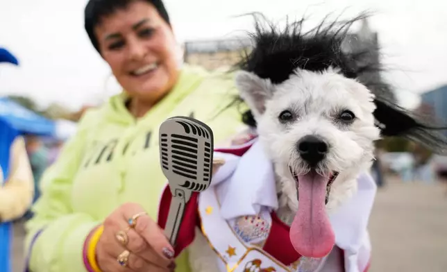 Michelle Dixon, of Laingsburg, holds her dog Abu, who is dressed as singer Elvis Presley, during an event for dog trick-or-treating, Friday, Oct. 17, 2025, in Lansing, Mich. (AP Photo/Ryan Sun)