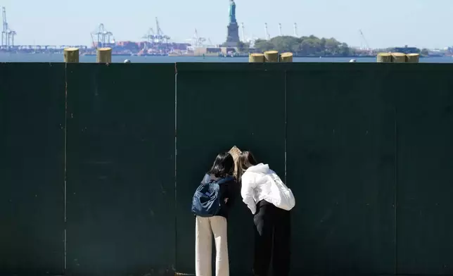 People look through fence to get a glance at the Statue of Liberty in New York, Wednesday, Oct. 1, 2025. (AP Photo/Seth Wenig)