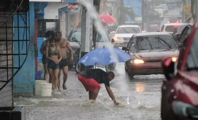 People walk in a street flooded by rains caused by Tropical Storm Melissa in Santo Domingo, Dominican Republic, Friday, Oct. 24, 2025. (AP Photo/Ricardo Hernandez)