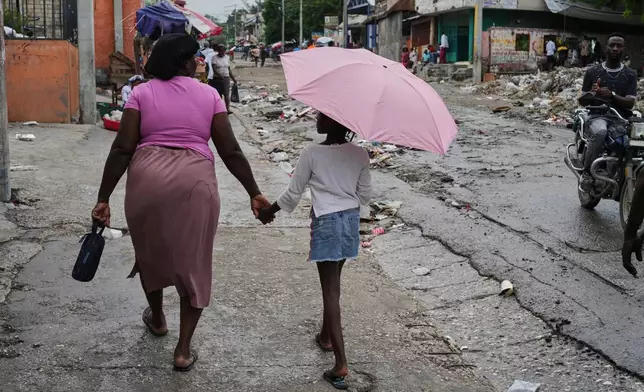 A woman holds a girl with an umbrella's hand during light rain in Port-au-Prince, Haiti, Thursday, Oct. 23, 2025. (AP Photo/Odelyn Joseph)