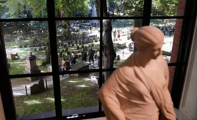 Visitors walk though the Granary Burying Ground, which includes the graves of John Hancock, Samuel Adams and Paul Revere, seen through a window at the Boston Athenaeum, Thursday, Oct. 9, 2025, in Boston. (AP Photo/Charles Krupa)