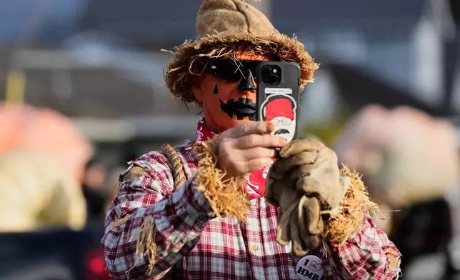 Norman Breshears, dressed up as a scarecrow, takes a photo of one of the giant pumpkins at the 52nd annual World Championship Pumpkin Weigh-Off in Half Moon Bay, Calif., Monday, Oct. 13, 2025. (AP Photo/Godofredo A. Vásquez)