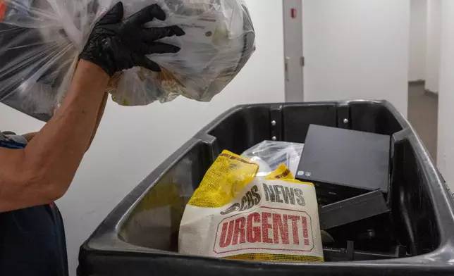 A cleaning person throws a bag of trash in a dumpster as members of the media pack up their belongings in the press area of the Pentagon, Wednesday, Oct. 15, 2025 in Washington. (AP Photo/Kevin Wolf)