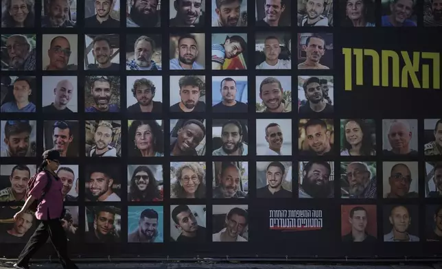 A woman walks past a banner with photographs of hostages who were kidnapped and held by Hamas in the Gaza Strip, in Jerusalem, Tuesday, Oct. 7, 2025, on the second anniversary of Hamas' cross-border attack on Israel on Oct. 7, 2023, which sparked the ongoing war in Gaza. (AP Photo/Leo Correa)