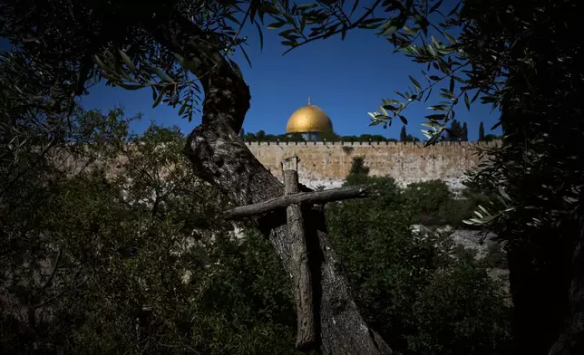 A cross hangs from an olive tree in the Franciscan hermitage on the Mount of Olives with the Dome of the Rock shrine at the Al-Aqsa Mosque compound in the background, in Jerusalem, Friday, Oct. 3, 2025. (AP Photo/Oded Balilty)