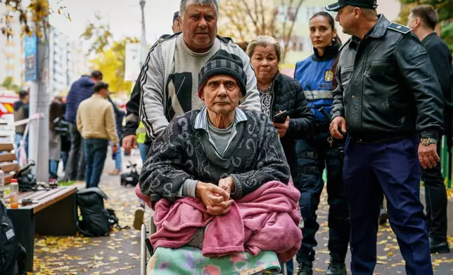An elderly resident of an apartment building which was heavily damaged after a powerful explosion, is pushed in a wheelchair by a man in Bucharest, Romania, Friday, Oct. 17, 2025. (AP Photo)