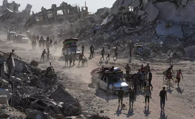 Displaced Palestinians with their belongings pass by destroyed buildings as they return to their homes in the Zeitoun neighborhood of Gaza City, Friday, Oct. 10, 2025, after Israel and Hamas agreed to pause their war and release remaining hostages. (AP Photo/Jehad Alshrafi)