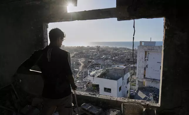 A man looks out from his damaged apartment at the destruction in his neighborhood in Gaza City, Friday, Oct. 10, 2025, after returning home following an agreement between Israel and Hamas on a ceasefire and the release of remaining hostages. (AP Photo/Jehad Alshrafi)