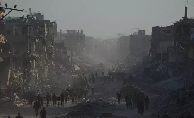 Displaced Palestinians carry their belongings as they walk along the heavily damaged Al-Jalaa Street in Gaza City, Saturday, Oct. 11, 2025, after Israel and Hamas agreed to a pause in their war and the release of the remaining hostages. (AP Photo/Abdel Kareem Hana)