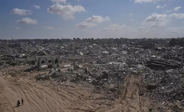 Two displaced Palestinians walk past destroyed buildings in the heavily damaged Sheikh Radwan neighborhood in Gaza City, Saturday, Oct. 11, 2025, after Israel and Hamas agreed to a pause in their war and the release of the remaining hostages. (AP Photo/Abdel Kareem Hana)
