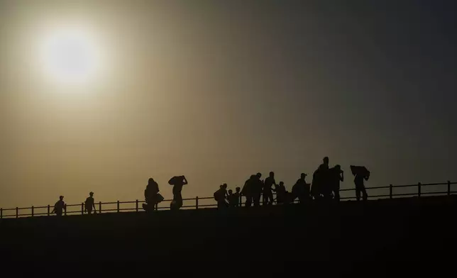 Displaced Palestinians carrying their belongings walk along the coastal road near Wadi Gaza in the central Gaza Strip at sunset, Friday, Oct. 10, 2025, after Israel and Hamas agreed to a pause in their war and the release of the remaining hostages. (AP Photo/Abdel Kareem Hana)