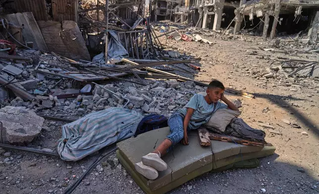 A Palestinian boy lies on a mattress amid the rubble of destroyed buildings in Khan Younis, southern Gaza Strip, Friday, Oct. 10, 2025, after Israel and Hamas agreed to a pause in their war and the release of the remaining hostages. (AP Photo/Jehad Alshrafi)