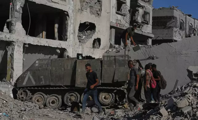 Palestinians inspect a damaged armored personnel carrier left behind by Israeli forces amid destroyed buildings in the Zeitoun neighborhood of Gaza City, Friday, Oct. 10, 2025, after Israel and Hamas agreed to pause their war and release the remaining hostages. (AP Photo/Jehad Alshrafi)