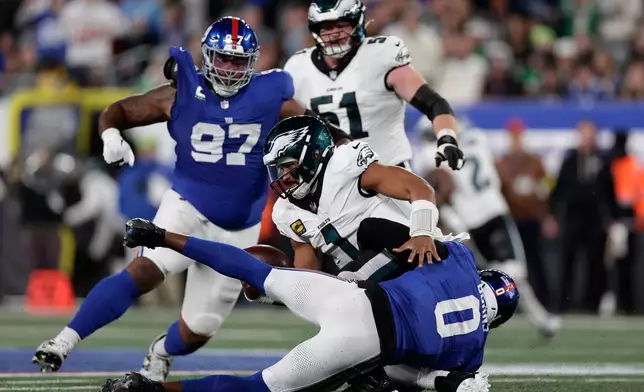 Philadelphia Eagles' Jalen Hurts (1) is sacked by New York Giants' Brian Burns (0) during the second half of an NFL football game Thursday, Oct. 9, 2025, in East Rutherford, N.J. (AP Photo/Adam Hunger)