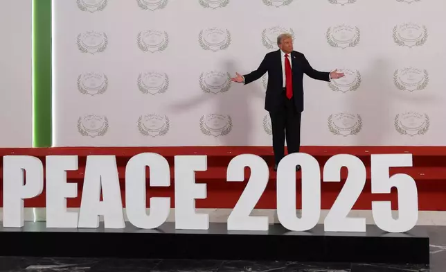 President Donald Trump gestures as he poses next to a sign before a family photo at a world leaders' summit on ending the Gaza war, in Sharm el-Sheikh, Egypt, Monday, Oct. 13, 2025. (Suzanne Plunkett, Pool Photo via AP)