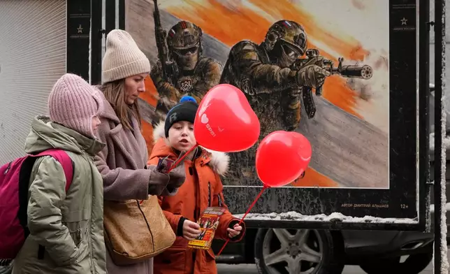 FILE - A woman with two children walks past a street exhibition of military posters named 'Together to Victory' dedicated to Russian army in St. Petersburg, Russia, Friday, Feb. 14, 2025. (AP Photo/Dmitri Lovetsky, File)