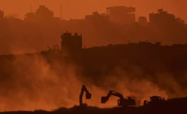 Israeli excavators work in the Gaza Strip as the sun sets, seen from southern Israel, Tuesday, Oct. 14, 2025. (AP Photo/Leo Correa)