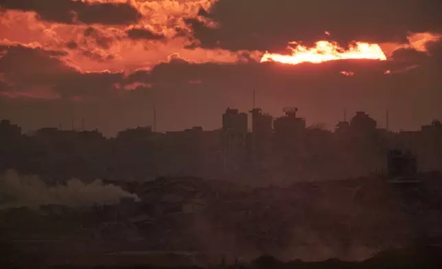 The sun sets behind buildings destroyed during Israeli ground and air operations in the northern Gaza Strip, as seen from southern Israel, Tuesday, Oct. 14, 2025. (AP Photo/Leo Correa)