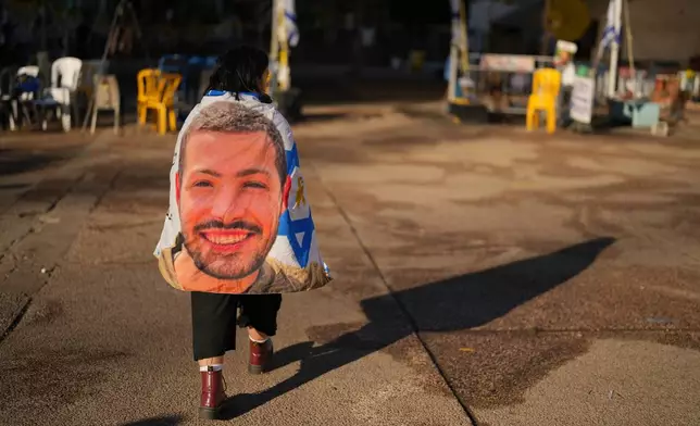 Israeli Yaar, only first name given, walks wrapped with an Israeli flag with the photo of one of her best friend Itay Chen, who was killed in Hamas' attack on Oct. 7, at the plaza known as hostages square, in Tel Aviv, Israel, Tuesday, Oct. 14, 2025. (AP Photo/Francisco Seco)