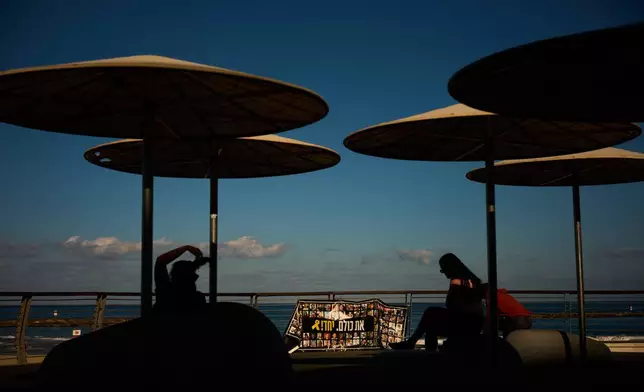 People sit in front of the sea alongside photographs of hostages who were held by Hamas in the Gaza Strip, in Tel Aviv, Israel, Tuesday, Oct. 14, 2025. (AP Photo/Emilio Morenatti)